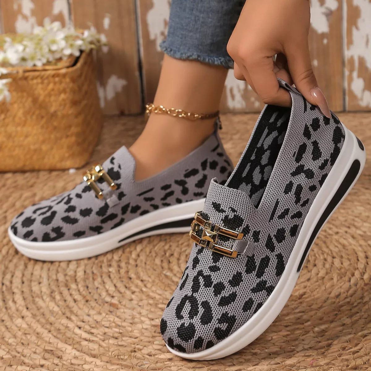 Gray slip-on shoes with black leopard print pattern worn by a person on a woven mat.