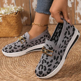 Gray slip-on shoes with black leopard print pattern worn by a person on a woven mat.