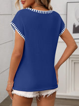 Woman wearing a royal blue short sleeve knit top with white contrast trim along the V-neckline and sleeves.