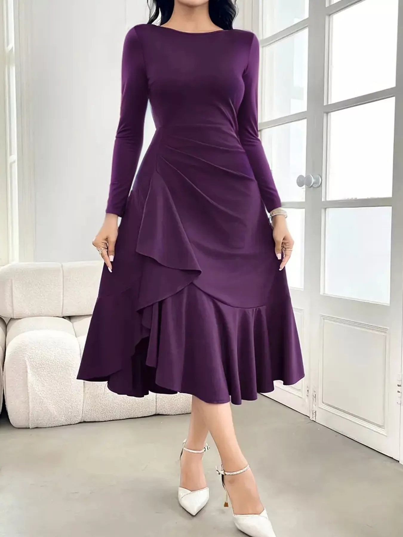 Woman wearing a purple dress with long sleeves in a room with a white sofa and glass door.