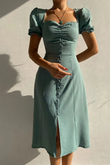 Woman wearing a sage sweetheart-neck midi dress with puff sleeves, ruched detailing, and a button-front slit.