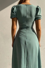 Woman wearing a sage sweetheart-neck midi dress with puff sleeves, ruched detailing, and a button-front slit.