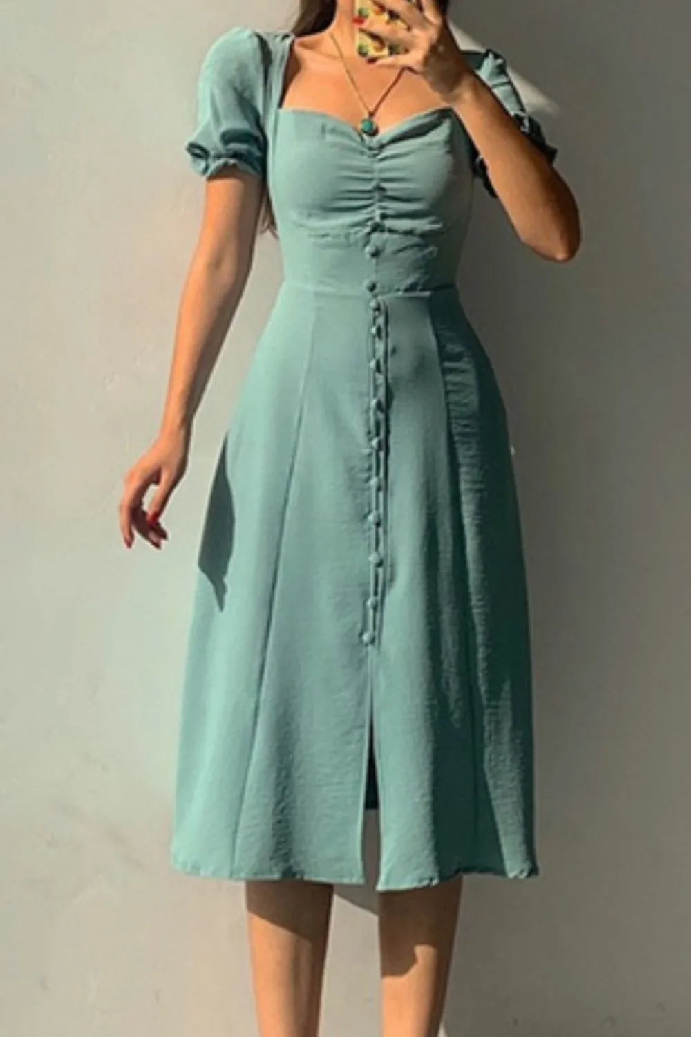 Woman wearing a sage sweetheart-neck midi dress with puff sleeves, ruched detailing, and a button-front slit.