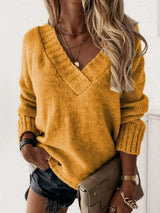 Woman wearing a sherbet V-neck long sleeve knit top with ribbed neckline and cuffs, styled with black denim shorts.