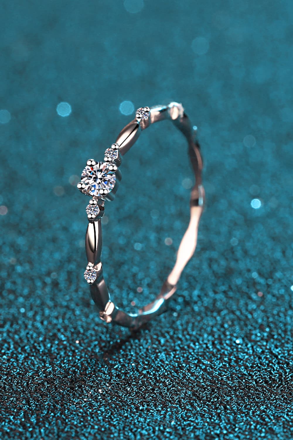 Rhodium-plated 925 sterling silver minimalist ring featuring a 0.1 carat round moissanite center stone with delicate sparkling accents on a teal background.