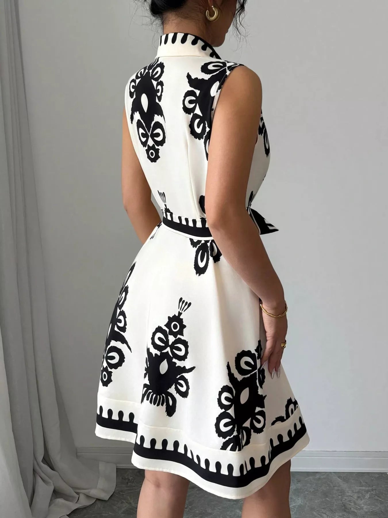 Person wearing a white dress with black geometric patterns against a plain background