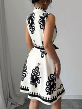 Person wearing a white dress with black geometric patterns against a plain background