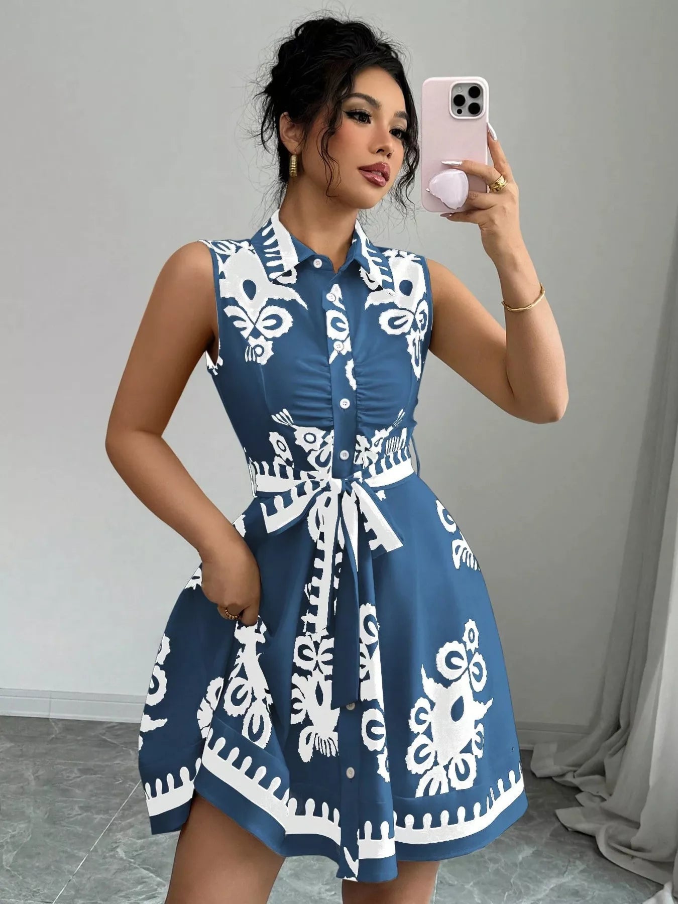 Woman wearing a blue dress with white patterns, taking a mirror selfie.