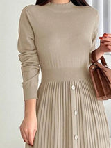 Woman wearing an apricot mock neck long sleeve knit midi dress with pleated skirt, front buttons and slit.