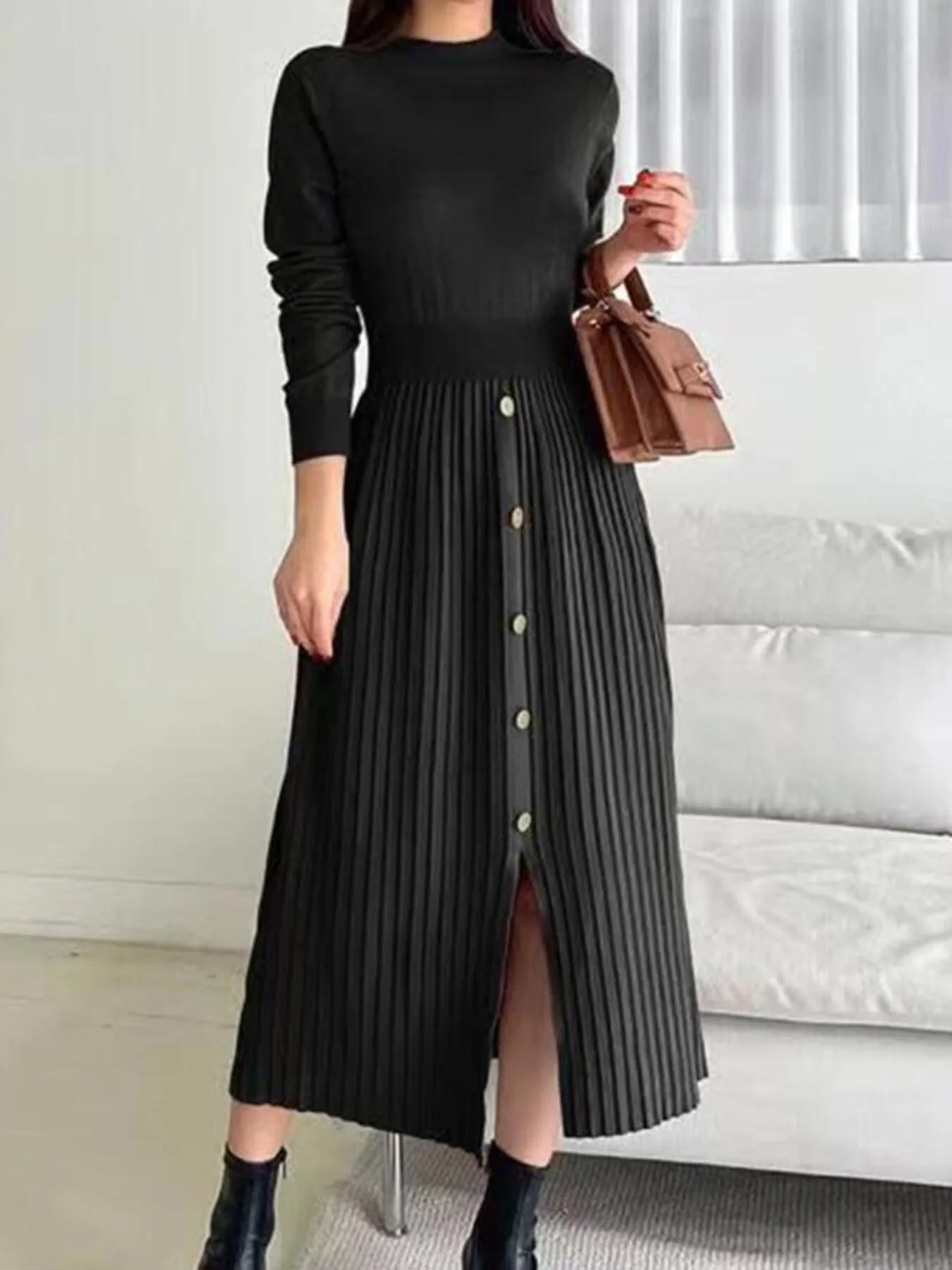 Woman wearing a black mock neck long sleeve knit midi dress with pleated skirt, front buttons and slit.