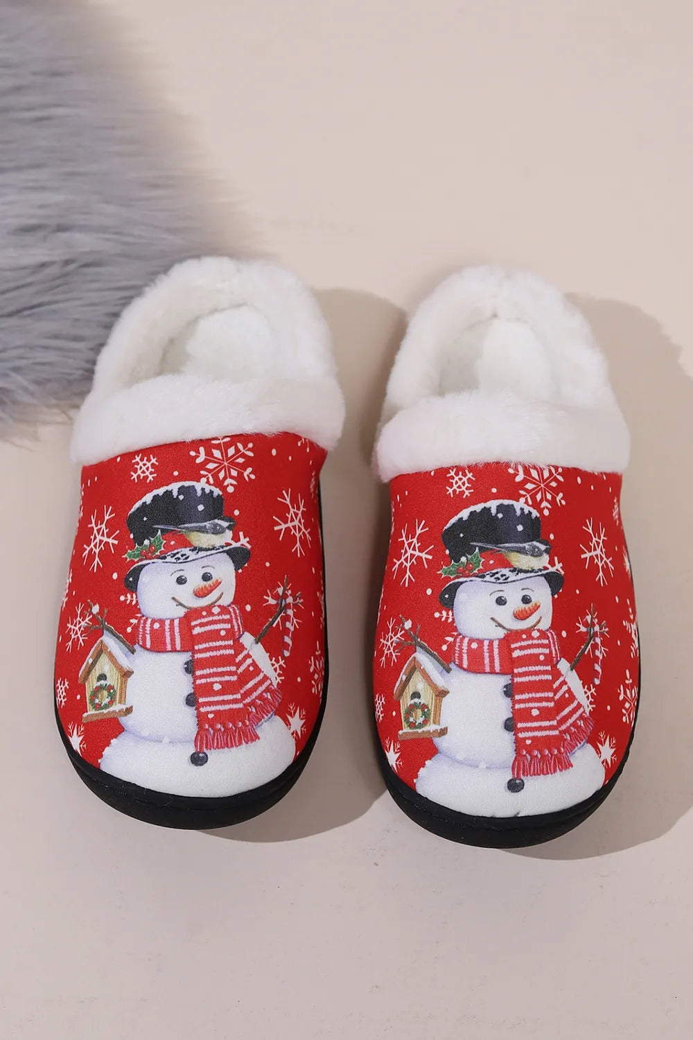 Red Christmas snowman slippers with fluffy white faux fur trim, snowflake pattern, round toe, and black flat soles, shown on feet.