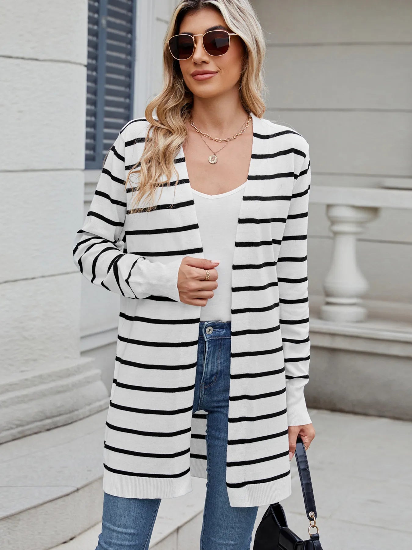 Woman wearing a black and white striped open front cardigan with blue jeans, layered over a white tank top for a casual everyday outfit.