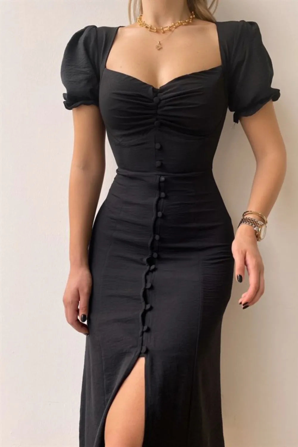 Woman wearing a black sweetheart-neck midi dress with puff sleeves, ruched detailing, and a button-front slit.