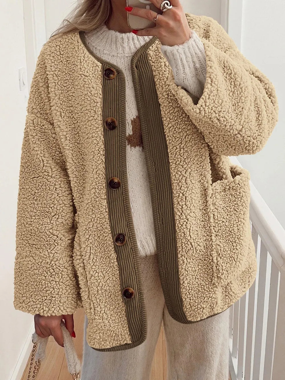 Women's tan sherpa jacket with contrasting ribbed trim, round neckline, front buttons, and patch pockets, layered over a cream sweater.