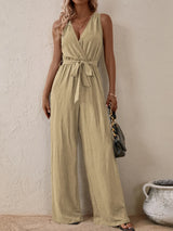 Woman wearing the Honey Tied Surplice Sleeveless Wide Leg Jumpsuit in tan with a tie waist and wide-leg silhouette, elegant women's one-piece outfit from Chic Mystik Boutique.