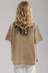Woman wearing an oversized taupe Basic Bae round-neck half-sleeve T-shirt styled with dark denim jeans and a long pendant necklace for a relaxed, casual look.