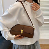 Taupe rectangular crossbody handbag with a gold turn-lock buckle and adjustable shoulder strap displayed on a modern tabletop.