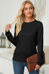 Woman wearing a black textured round neck long sleeve blouse with dark-wash jeans and brown clutch.