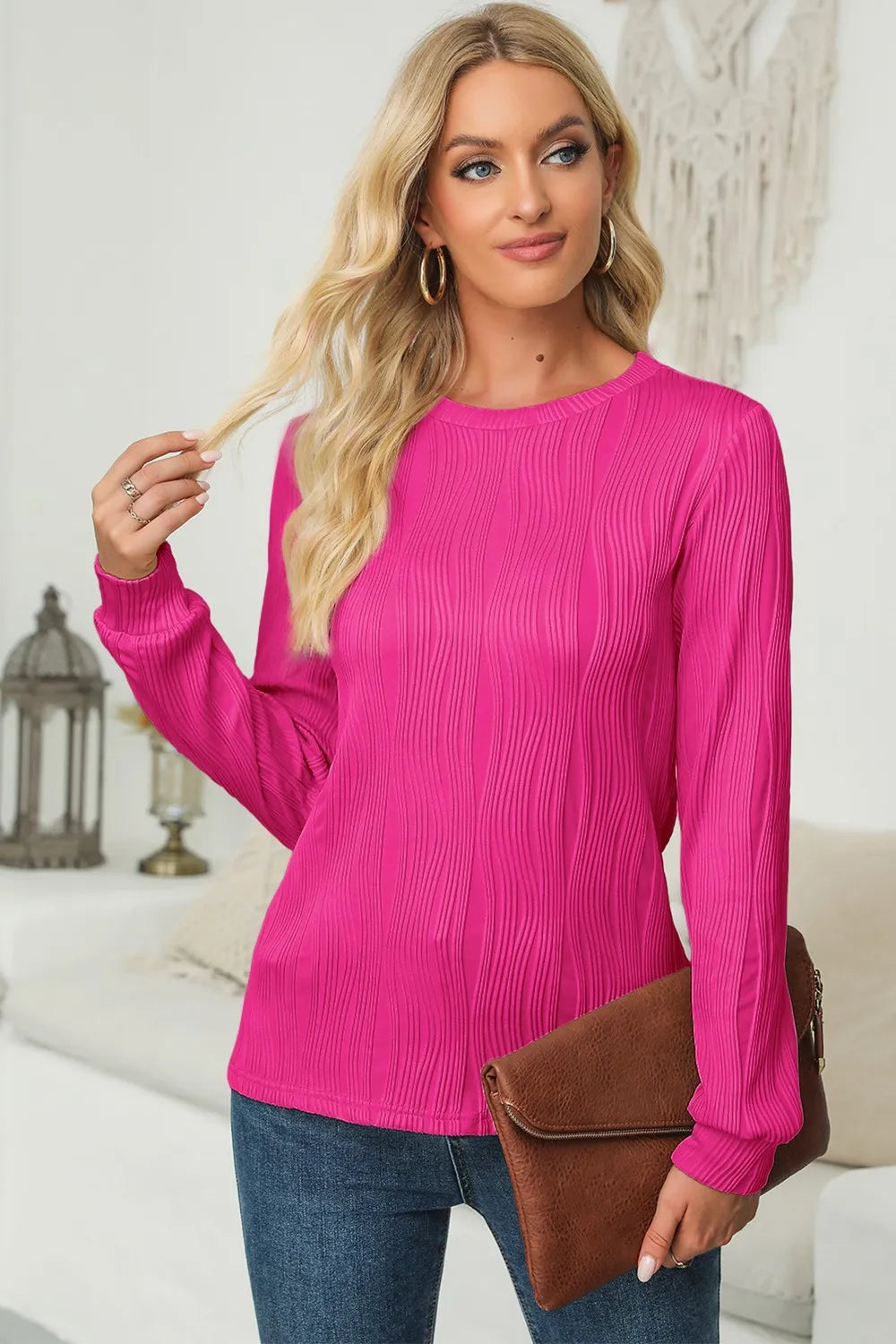 Woman wearing a cerise textured round neck long sleeve blouse with dark-wash jeans and brown clutch.