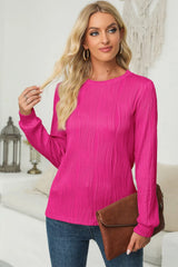 Woman wearing a cerise textured round neck long sleeve blouse with dark-wash jeans and brown clutch.