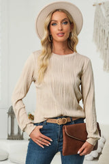Woman wearing a dust storm textured round neck long sleeve blouse with dark-wash jeans, brown clutch and cream hat.