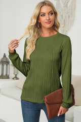 Woman wearing a moss textured round neck long sleeve blouse with dark-wash jeans and brown clutch.