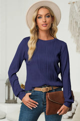 Woman wearing a navy textured round neck long sleeve blouse with dark-wash jeans, brown clutch and cream hat.
