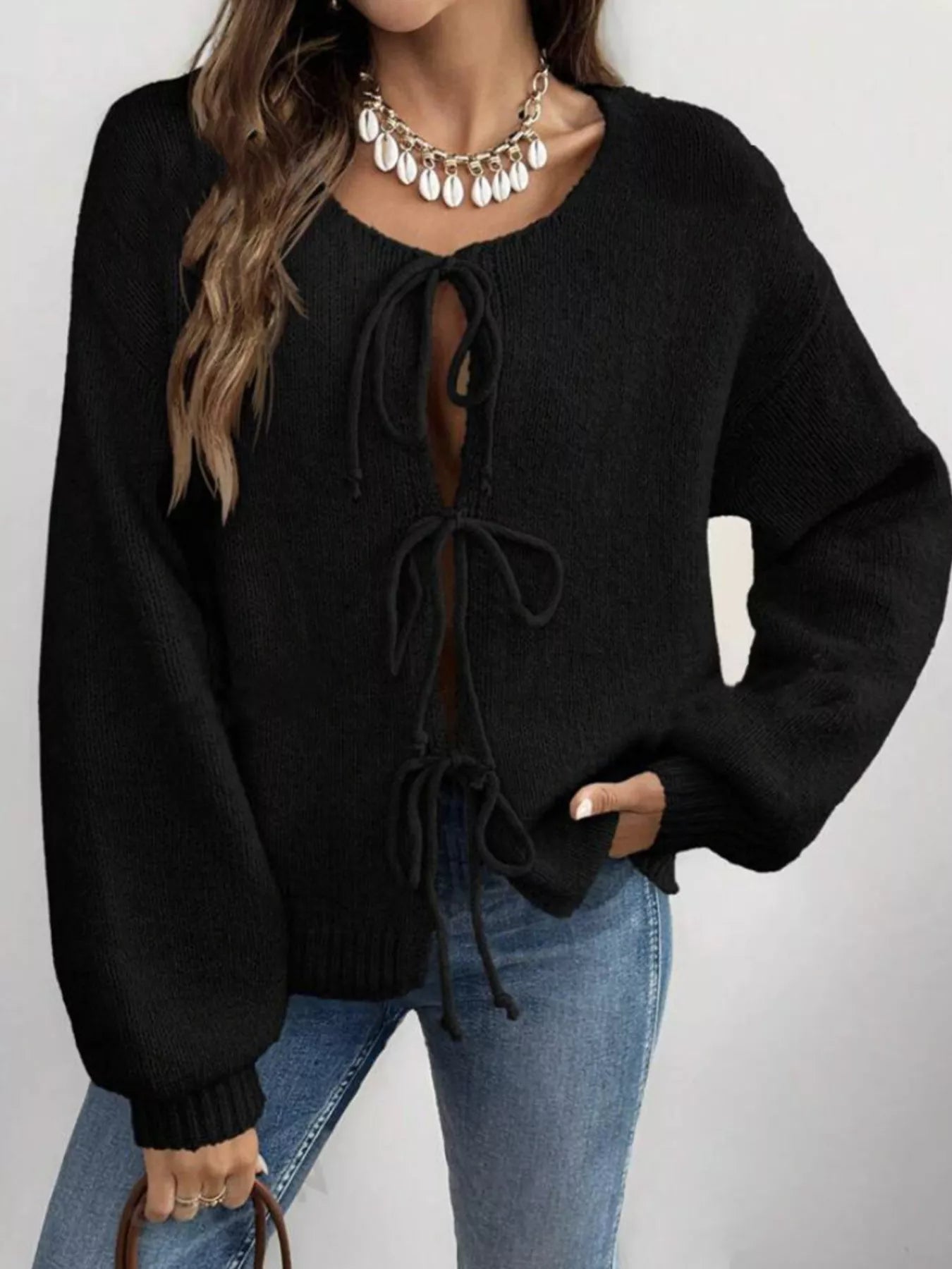 Woman wearing a black tie-front long sleeve knit cardigan with three bow ties paired with blue jeans.