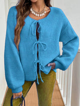 Woman wearing a sky-blue tie-front long sleeve knit cardigan with three bow ties paired with blue jeans.