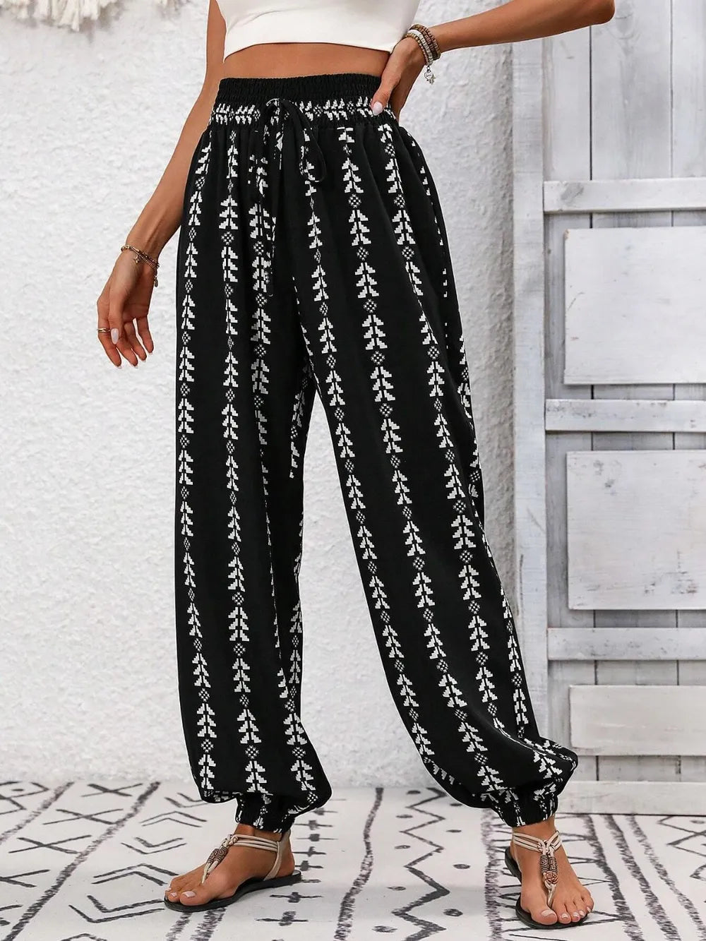 Black pants with white floral pattern worn by a person against a light gray wall. front side view