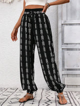 Black pants with white floral pattern worn by a person against a light gray wall. front side view