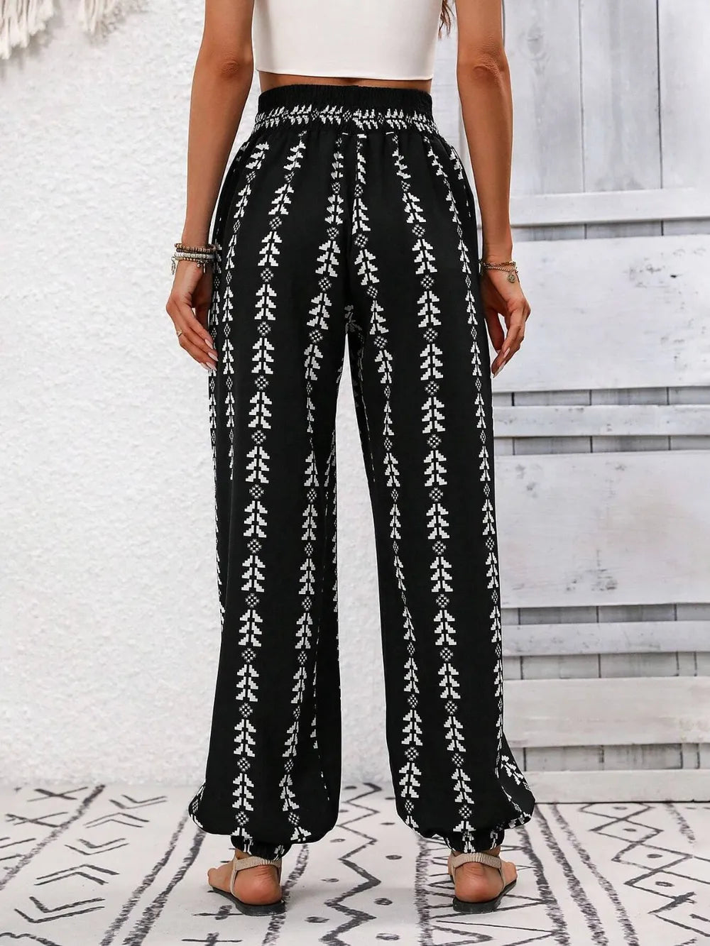 Person wearing black patterned pants with a white top on a light wooden floor. back view