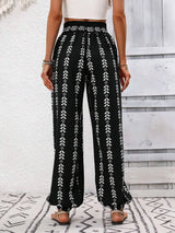 Person wearing black patterned pants with a white top on a light wooden floor. back view