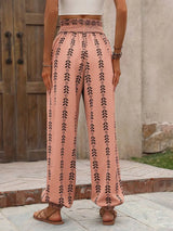 Person wearing pink patterned pants standing outdoors with a wooden door and stone wall in the background.