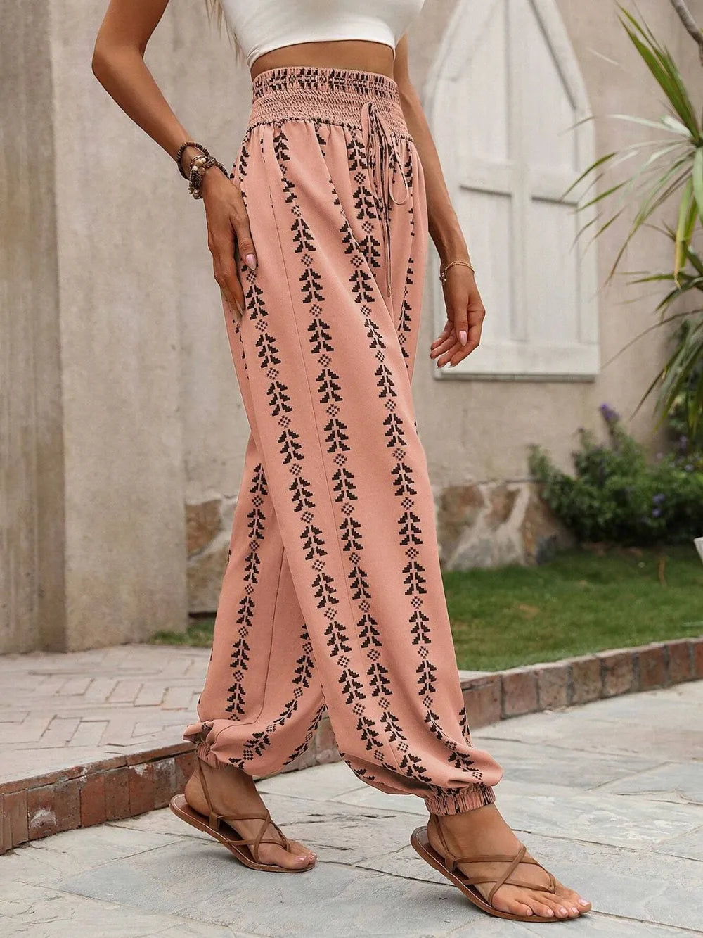 Person wearing burnt coral pants with black patterns and sandals, standing outdoors. side view