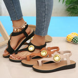 Black and brown sandals with gold accents worn by a person on a light background