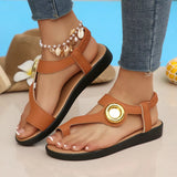Brown sandals with a gold button detail worn by a person on a light background