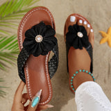 Brown sandals with black floral decorations held by a person with a starfish and palm leaf in the background.