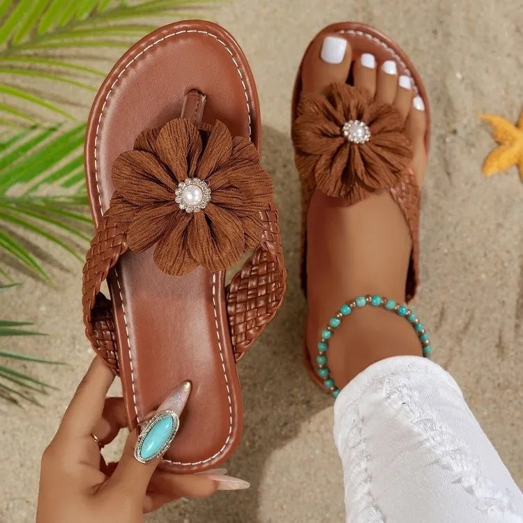 Brown sandals with decorative flowers on a sandy background