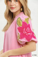 Woman wearing a light pink top with floral embroidery on a white background