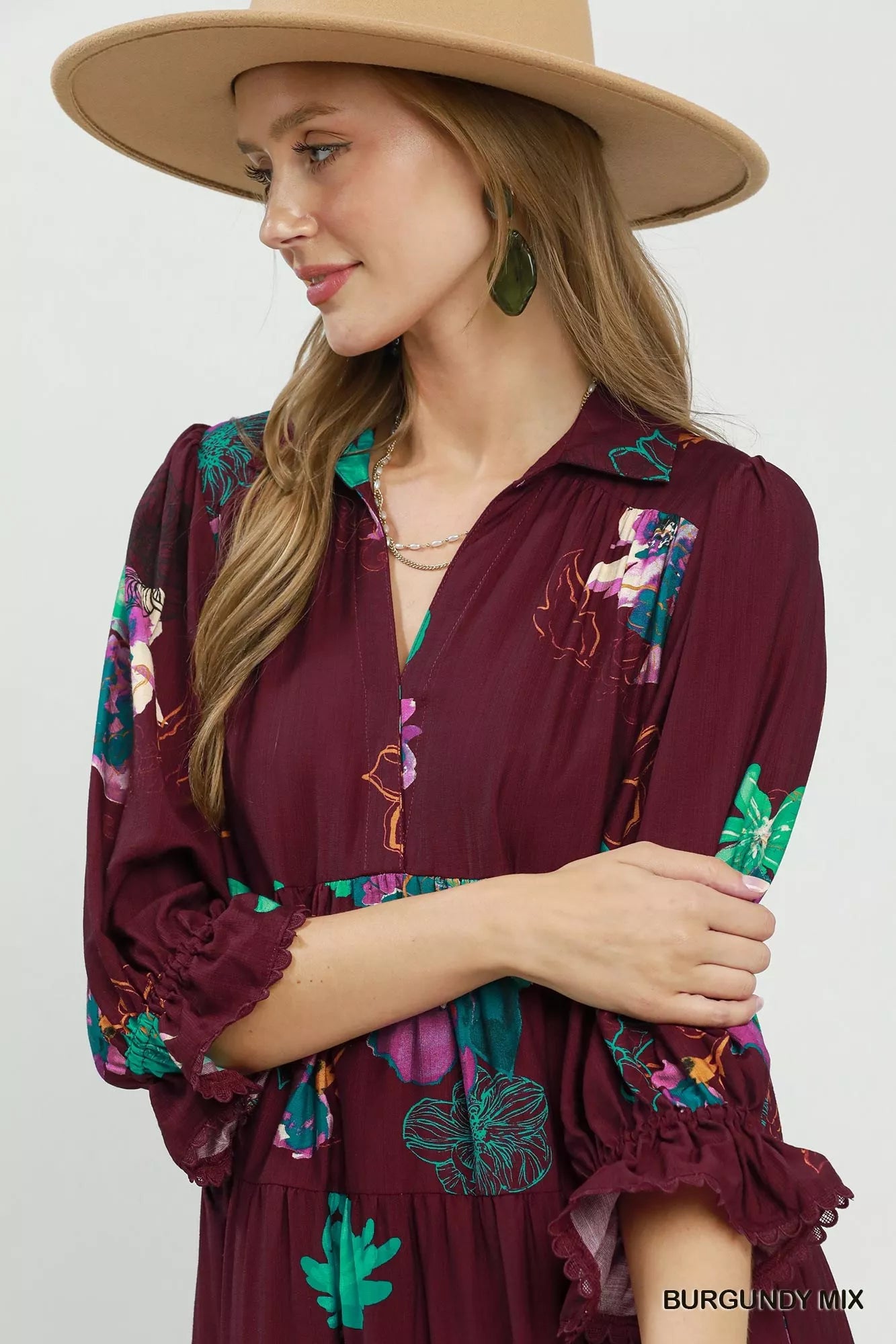 Woman wearing a burgundy dress with colorful embroidery and a beige hat on a white background