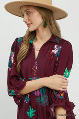 Woman wearing a burgundy dress with colorful embroidery and a beige hat on a white background