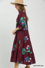 Woman wearing a burgundy dress with floral embroidery and a beige hat on a white background