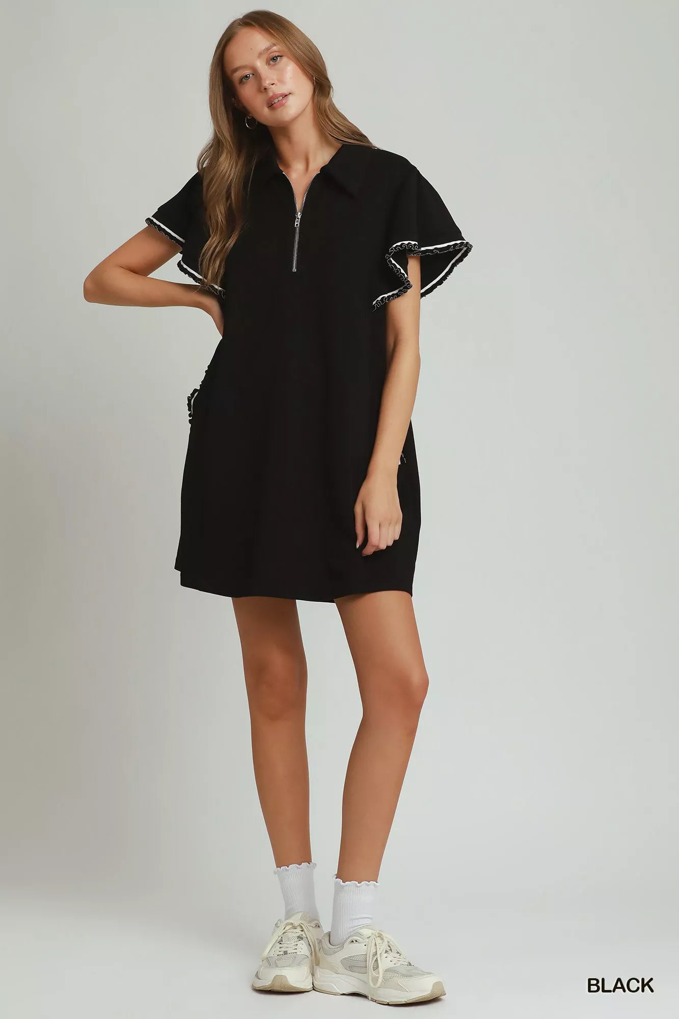 Woman wearing a black dress with white trim on a plain background