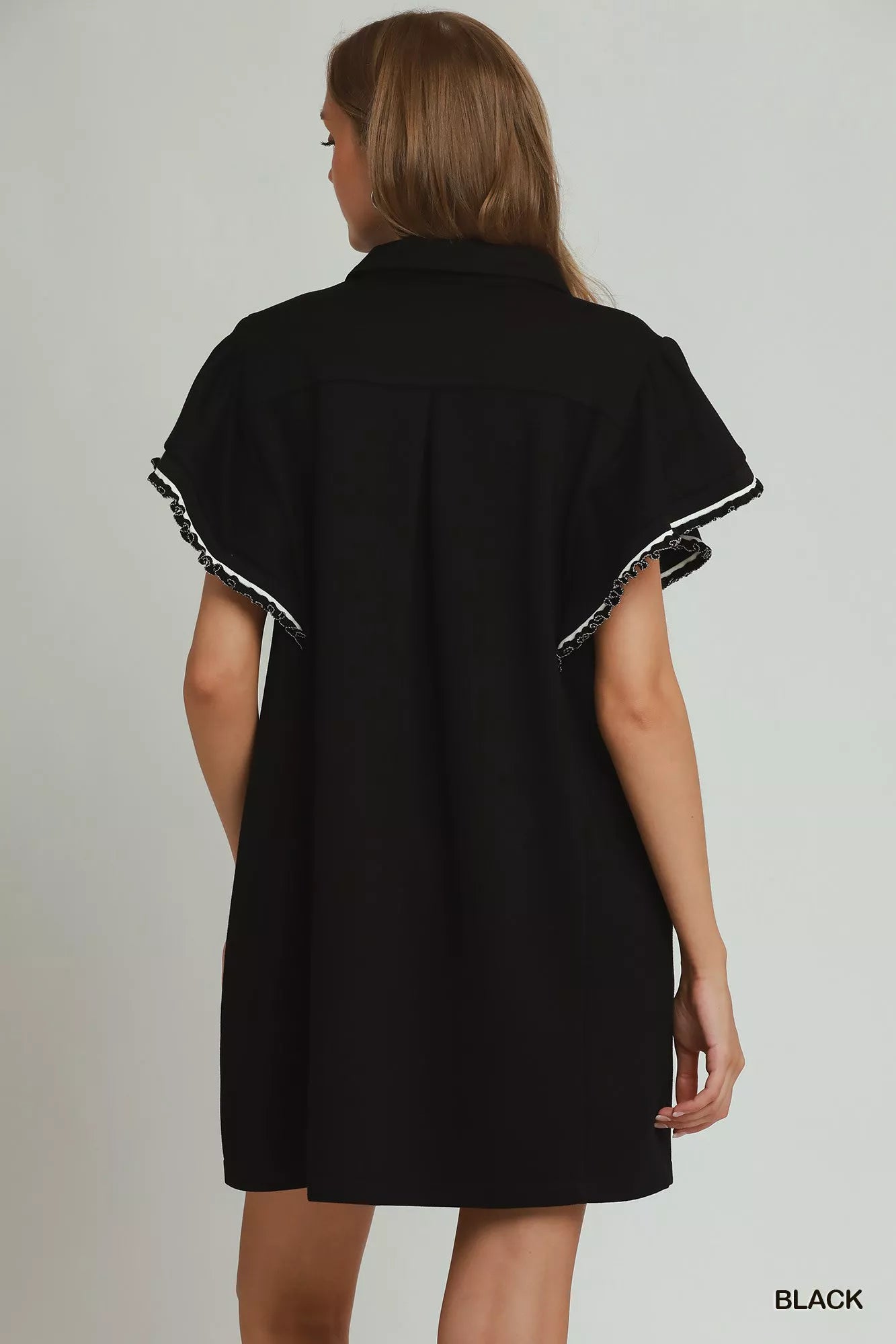 Black dress with white trim worn by a model on a plain background