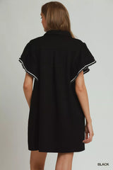 Black dress with white trim worn by a model on a plain background