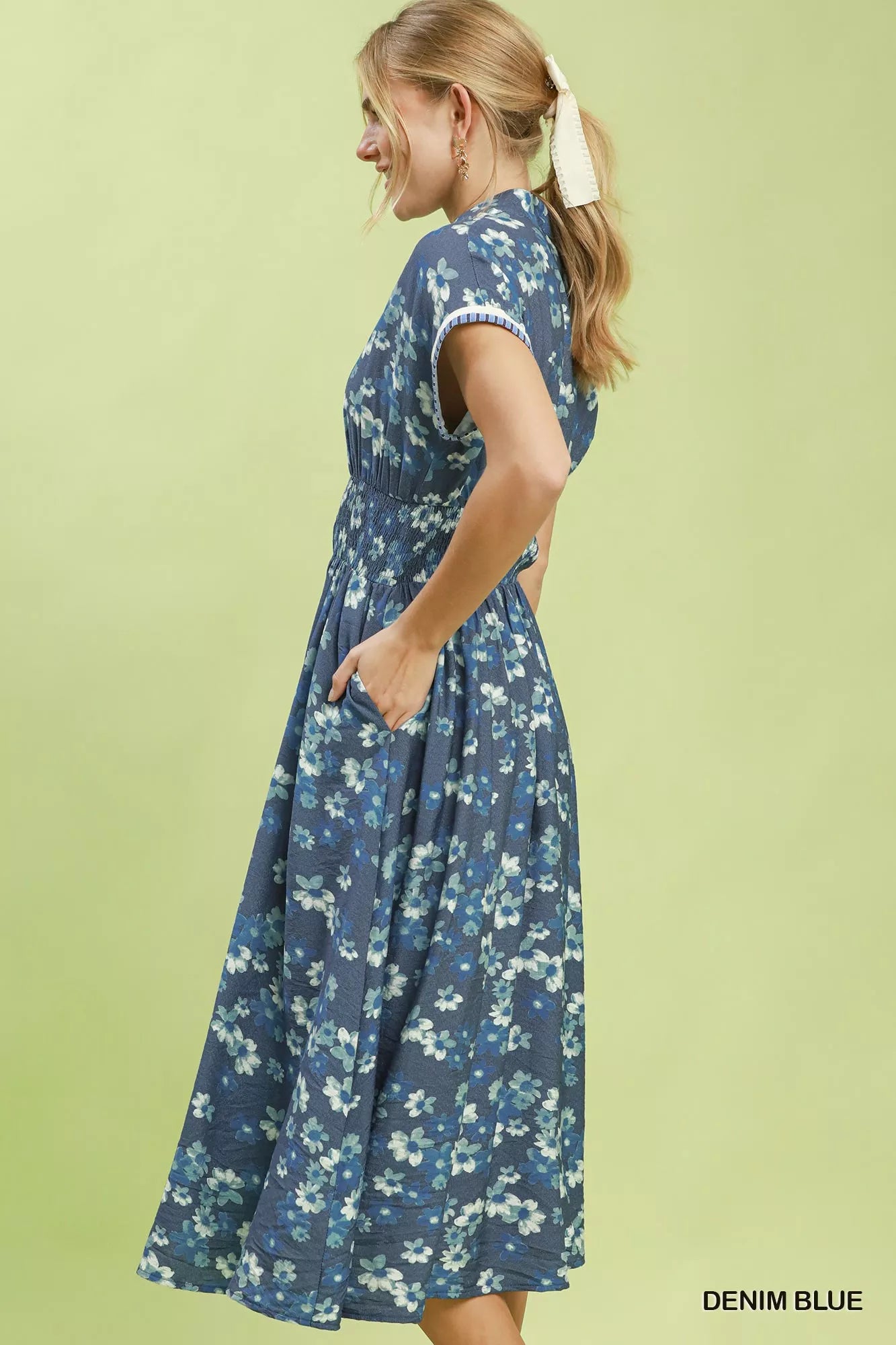 Woman wearing a denim blue floral dress against a light green background
