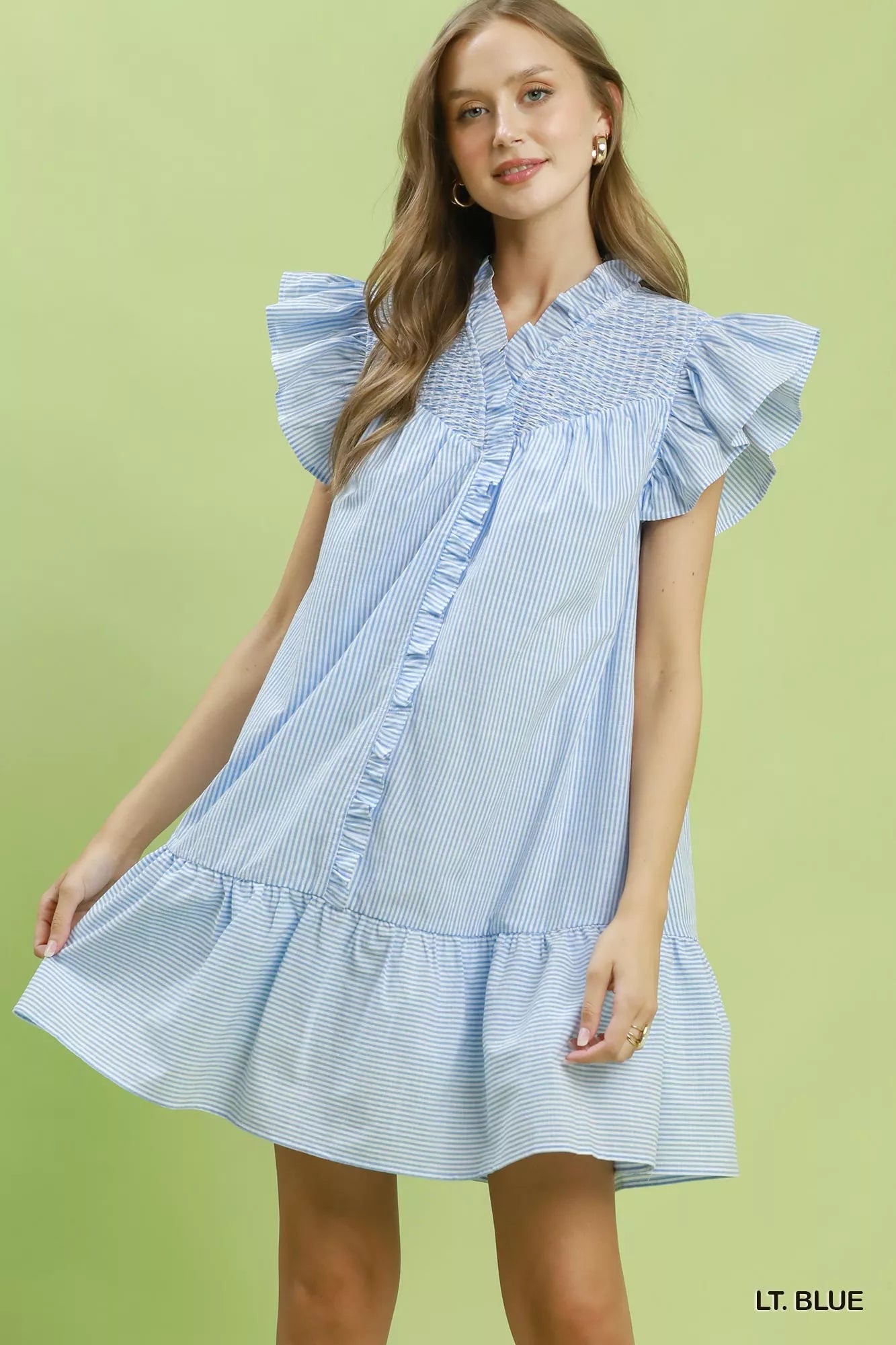Woman wearing a light blue dress with ruffled sleeves on a green background