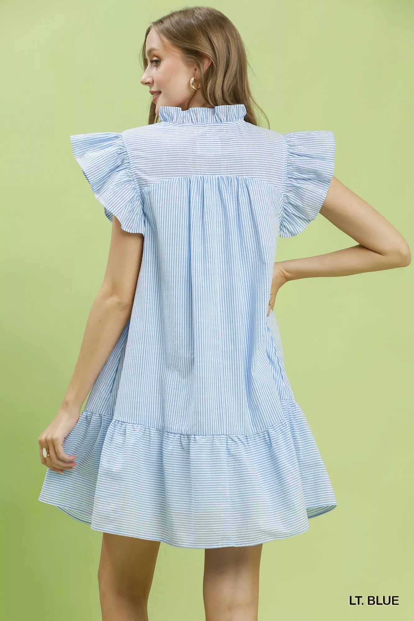 Woman wearing a light blue dress with ruffled sleeves on a green background