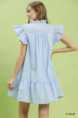 Woman wearing a light blue dress with ruffled sleeves on a green background